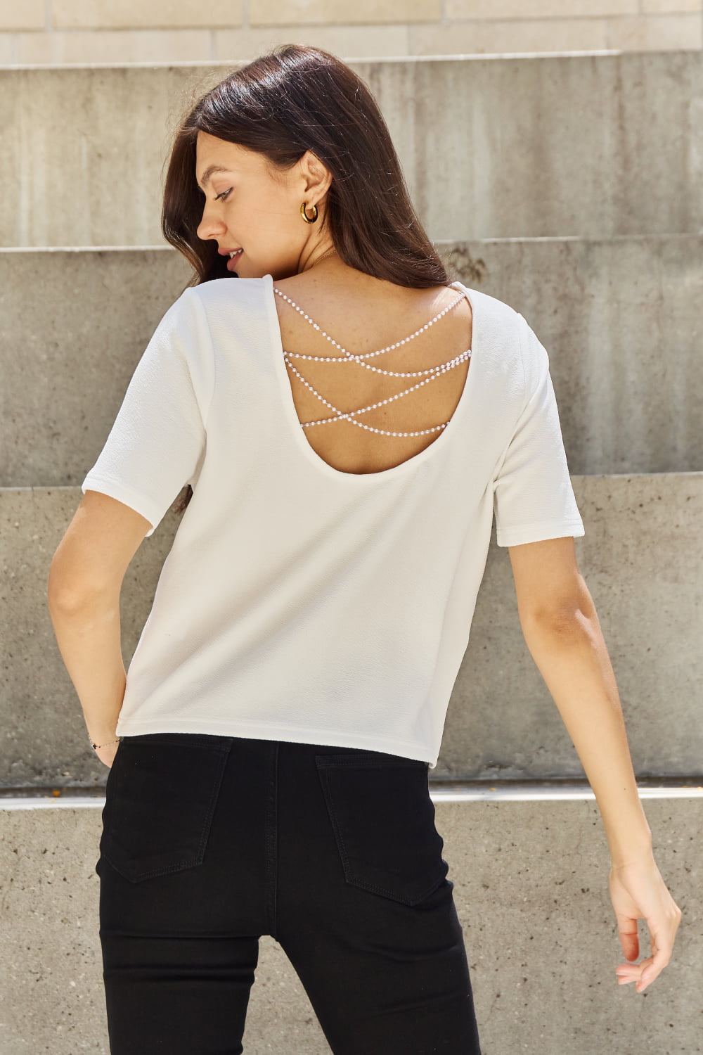 woman standing with back toward me, wearing white t-shirt with pearl detail drape across open back
