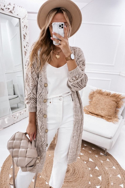 woman standing indoors wearing an all white outfit and beige longline knit cardigan