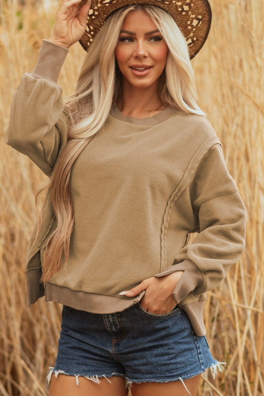 woman wearing beige color sweatshirt with raw hem details, paired with cut off jean shorts, and boho style sunhat, standing in wheat field