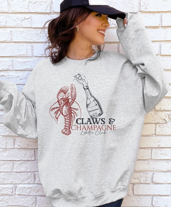 woman wearing grey graphic sweatshirt with lobster and champagne bottle standing in front of white brick wall