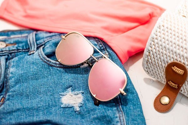pink aviator sunglasses laying on top of jean shorts 