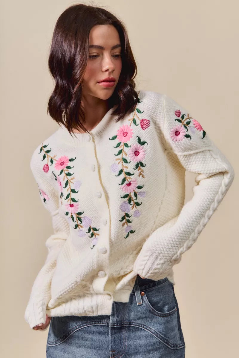 Woman wearing a cream-colored cardigan with floral embroidery on a beige background