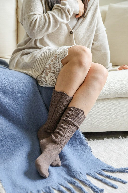 Person wearing brown knee-high socks sitting on a couch with a blue blanket.