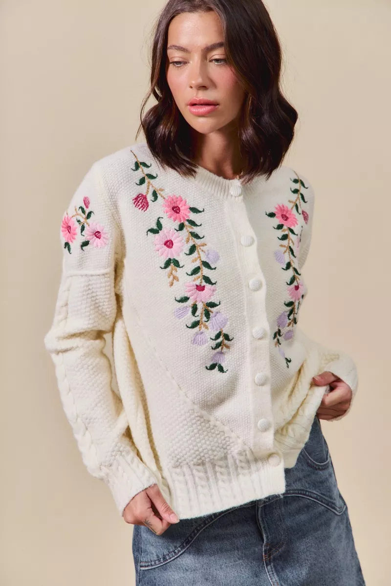 Woman wearing a cream-colored cardigan with floral embroidery on a beige background