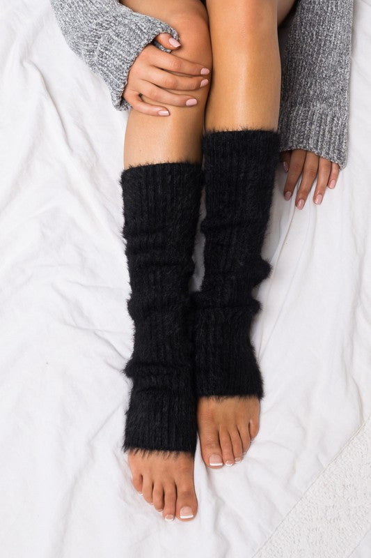 Person wearing black knitted leg warmers on a white background