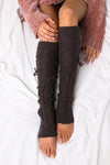 Person wearing dark gray cable knit leg warmers on a white surface
