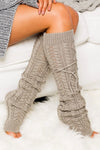 Person wearing beige knitted leg warmers on a white surface