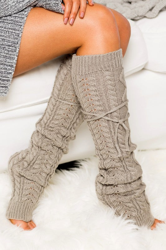 Person wearing beige knitted leg warmers on a white surface