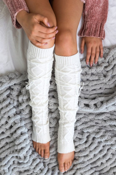 Person wearing white cable knit leg warmers on a textured surface