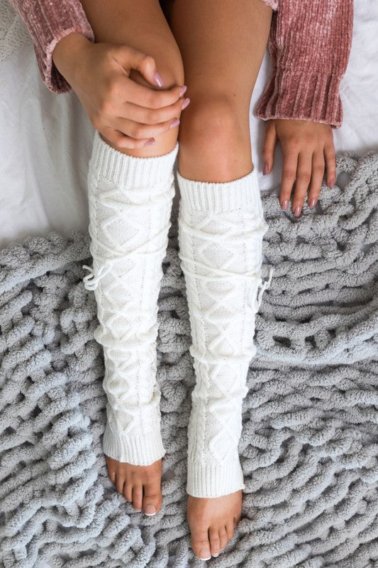 Person wearing white cable knit leg warmers on a textured surface