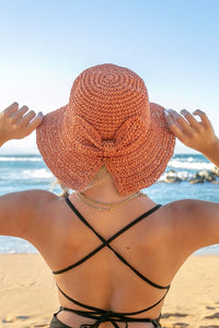 Person wearing a large pink sun hat on a beach with ocean view