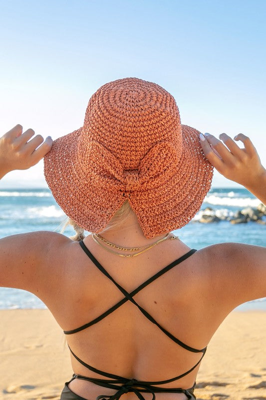 Person wearing a large pink sun hat on a beach with ocean view
