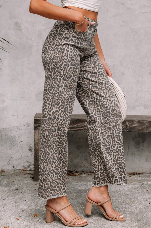 Person wearing leopard print pants and a white top, standing against a gray wall.
