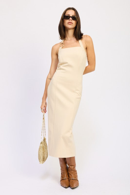Woman wearing a beige dress with brown boots and sunglasses on a white background