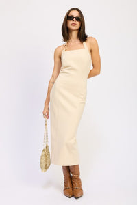 Woman wearing a beige dress with brown boots and sunglasses on a white background