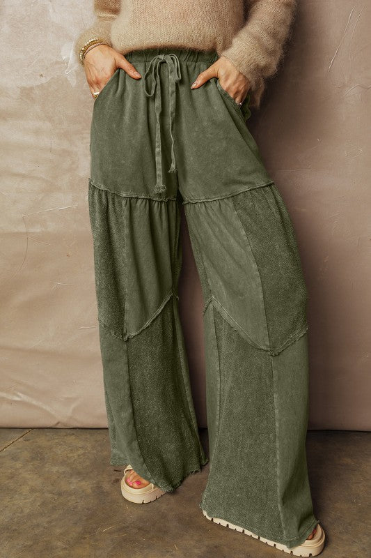 Person wearing olive green layered pants against a beige wall.