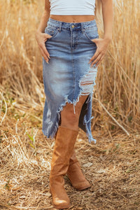 Person wearing a distressed denim skirt and brown knee-high boots in a field.