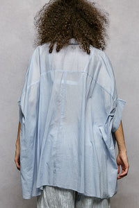 Back view of a model wearing a sky blue 100% cotton POL button-down shirt with a high-low hem.