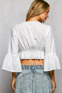 White cotton cropped V-neck blouse with flared ruffle sleeves and elastic waistband.