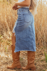 Person wearing a denim skirt and brown boots standing in a field of tall grass.