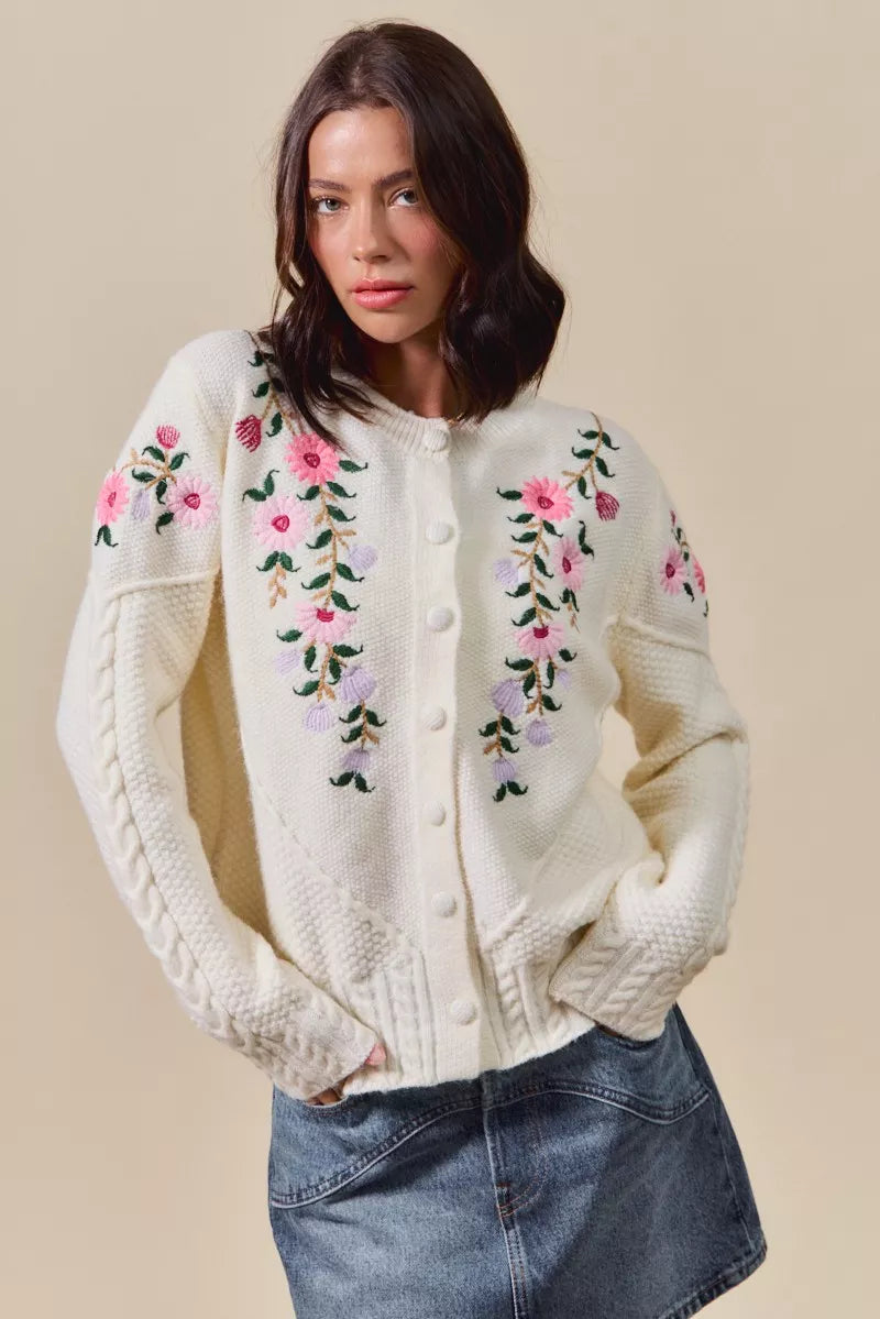 Woman wearing a cream-colored cardigan with floral embroidery on a beige background