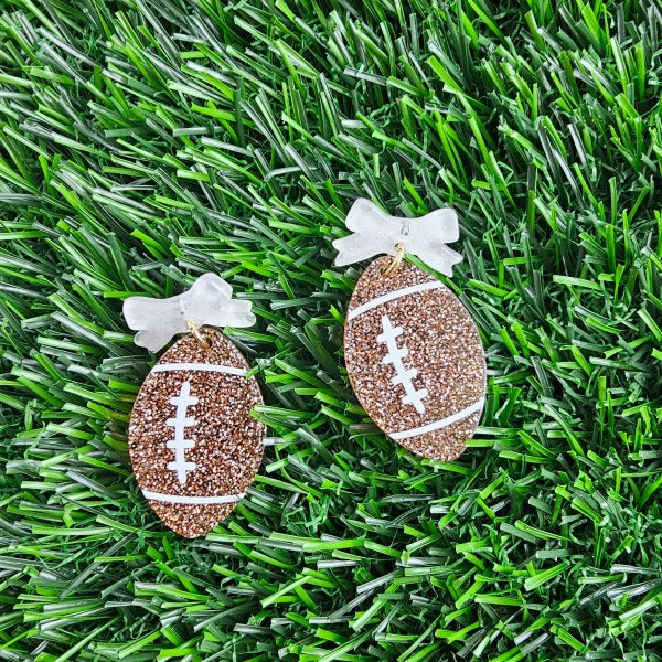 Bow Football Earrings-Football Season Must-have Earrings. Cheer in style with our Game Day Bow Football Earrings! Featuring a dainty white bow paired with a glittery brown football.