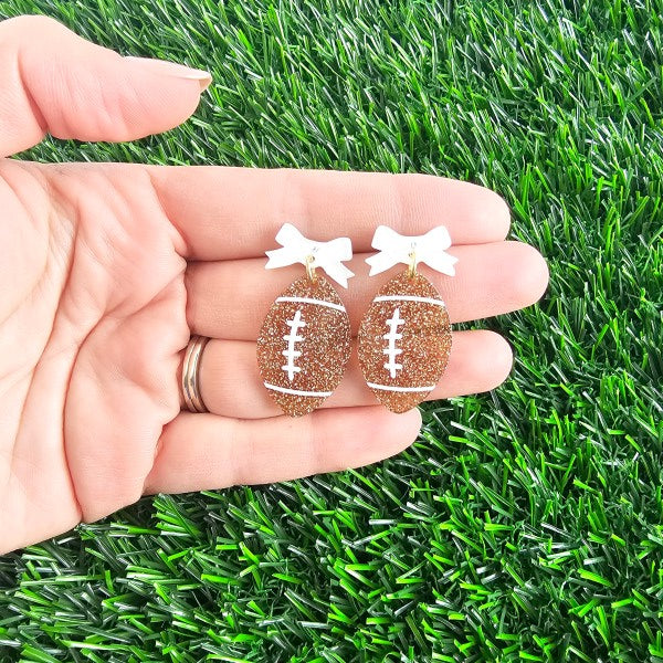Bow Football Earrings-Football Season Must-have Earrings. Cheer in style with our Game Day Bow Football Earrings! Featuring a dainty white bow paired with a glittery brown football.