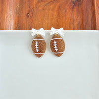 Bow Football Earrings-Football Season Must-have Earrings. Cheer in style with our Game Day Bow Football Earrings! Featuring a dainty white bow paired with a glittery brown football.