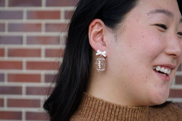 Bow Football Earrings-Football Season Must-have Earrings. Cheer in style with our Game Day Bow Football Earrings! Featuring a dainty white bow paired with a glittery brown football.