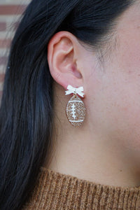 Bow Football Earrings-Football Season Must-have Earrings. Cheer in style with our Game Day Bow Football Earrings! Featuring a dainty white bow paired with a glittery brown football.