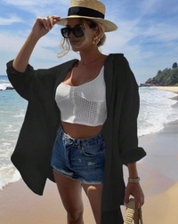 Woman on a beach wearing a white crochet top, denim shorts, and a straw hat.