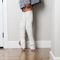 Person wearing white ribbed leg warmers standing against a white wall.