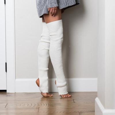Person wearing white ribbed leg warmers standing against a white wall.