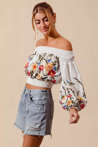 Woman wearing a floral off-shoulder top and denim shorts on a beige background