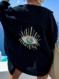 Black cover up with a decorative sequins evil eye design worn by a person, with a scenic background.