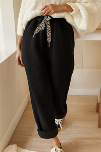 Person wearing black pants with a leopard print scarf, standing indoors.