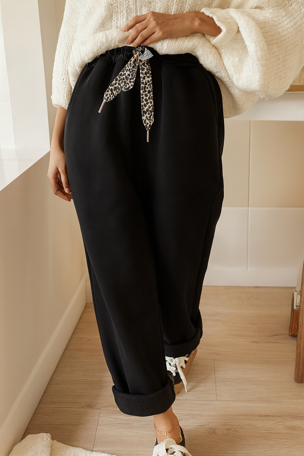 Person wearing black pants with a leopard print scarf, standing indoors.