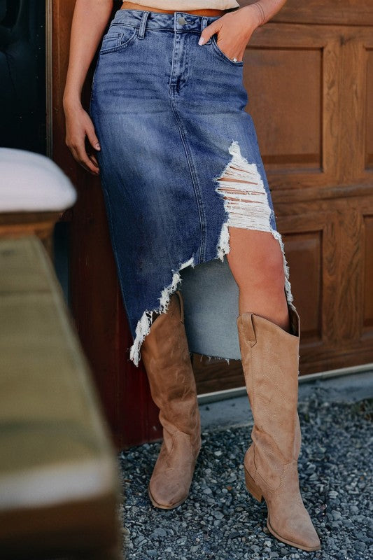 Person wearing a ripped denim skirt and tan knee-high boots in an outdoor setting.