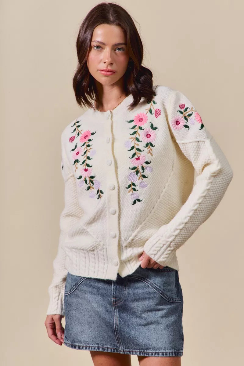 Woman wearing a cream-colored cardigan with floral embroidery on a beige background