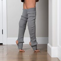 Person wearing gray ribbed leg warmers on a wooden floor.