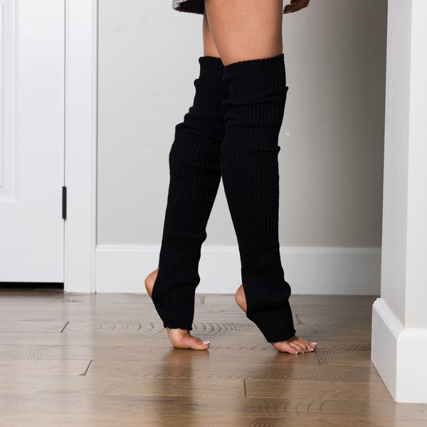 Person wearing black ribbed leg warmers on a wooden floor.