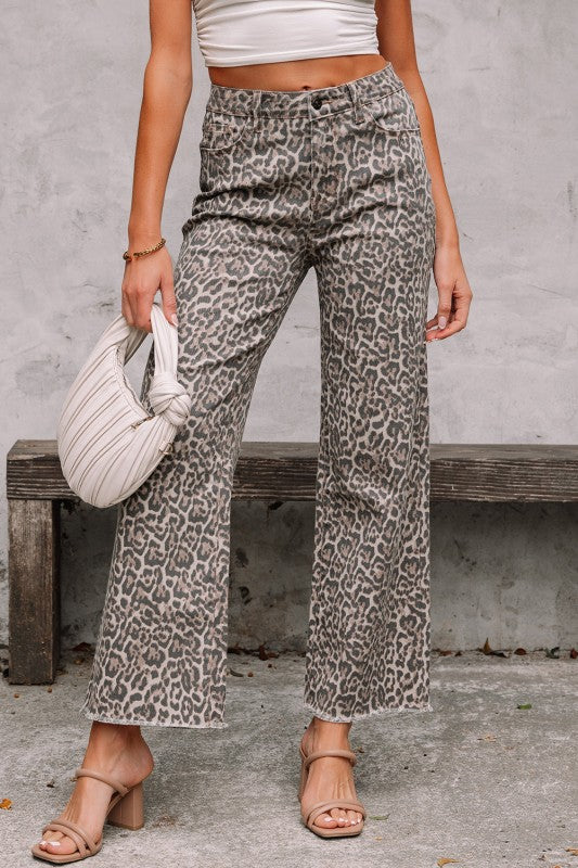 Person wearing leopard print pants with a white top and beige sandals, holding a white handbag.