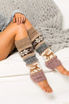 Leg warmers with deer pattern worn by a person sitting on a white surface with a gray textured blanket.