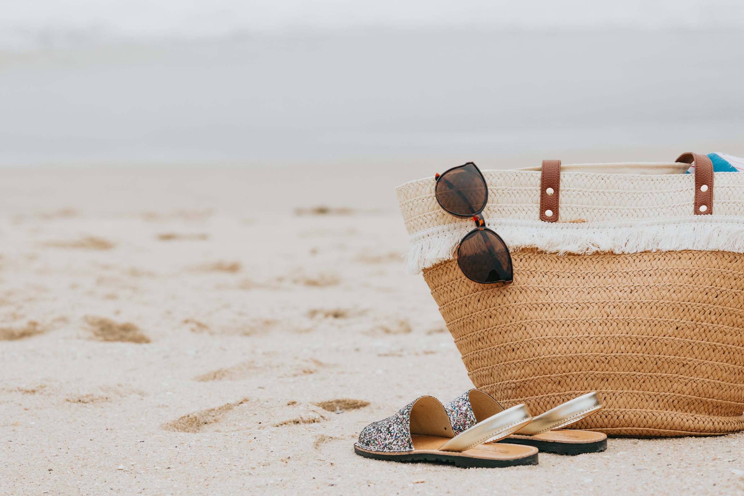 sandy beach with sandals, sunglasses, and woven beach bag