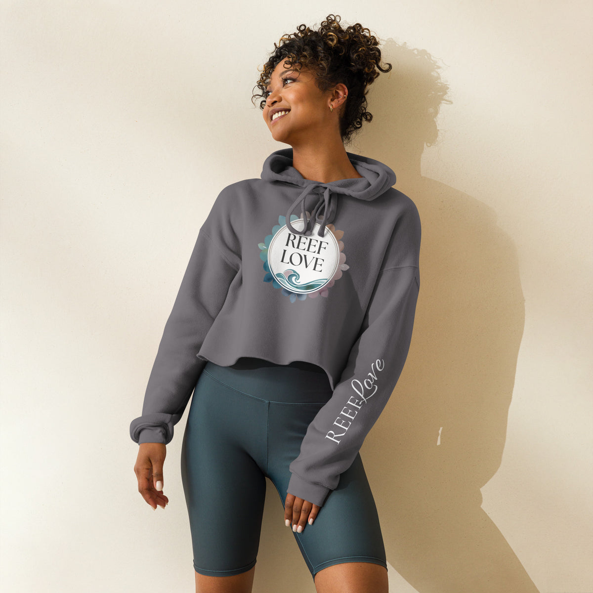 Woman wearing a gray hoodie and teal shorts with 'Reef Love' branding on a beige background